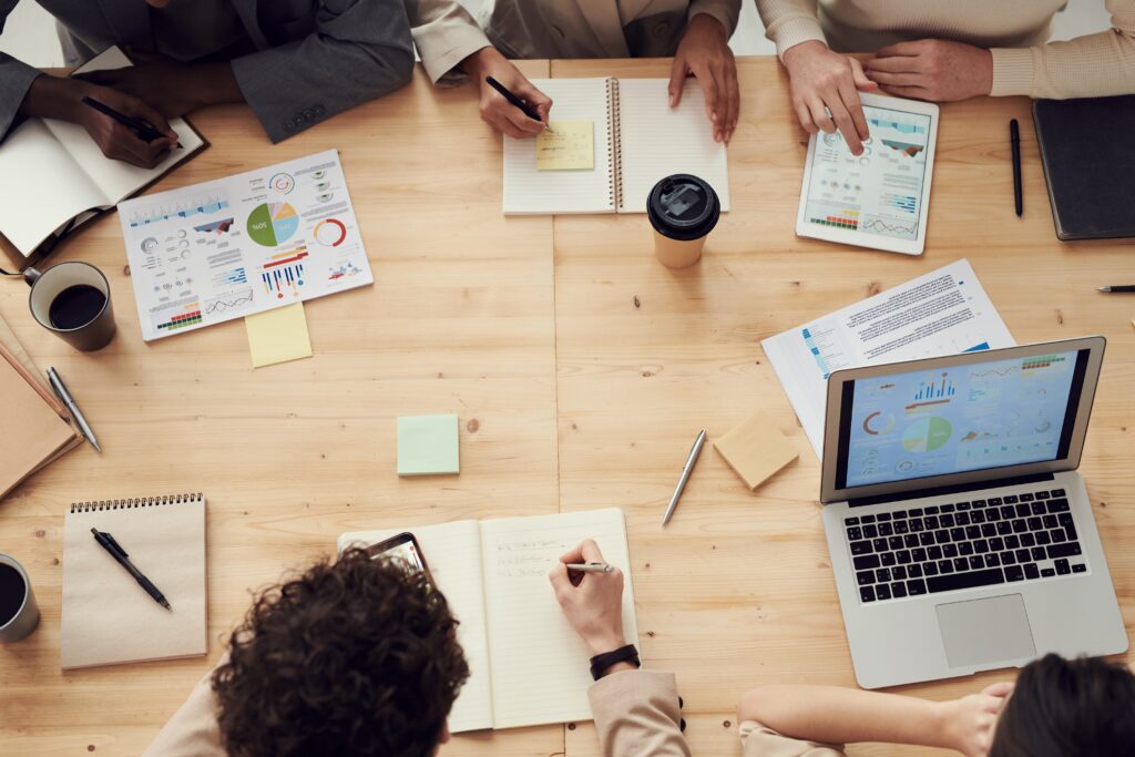Professionals collaboratively working at a table with laptops, documents, and charts during a business meeting.