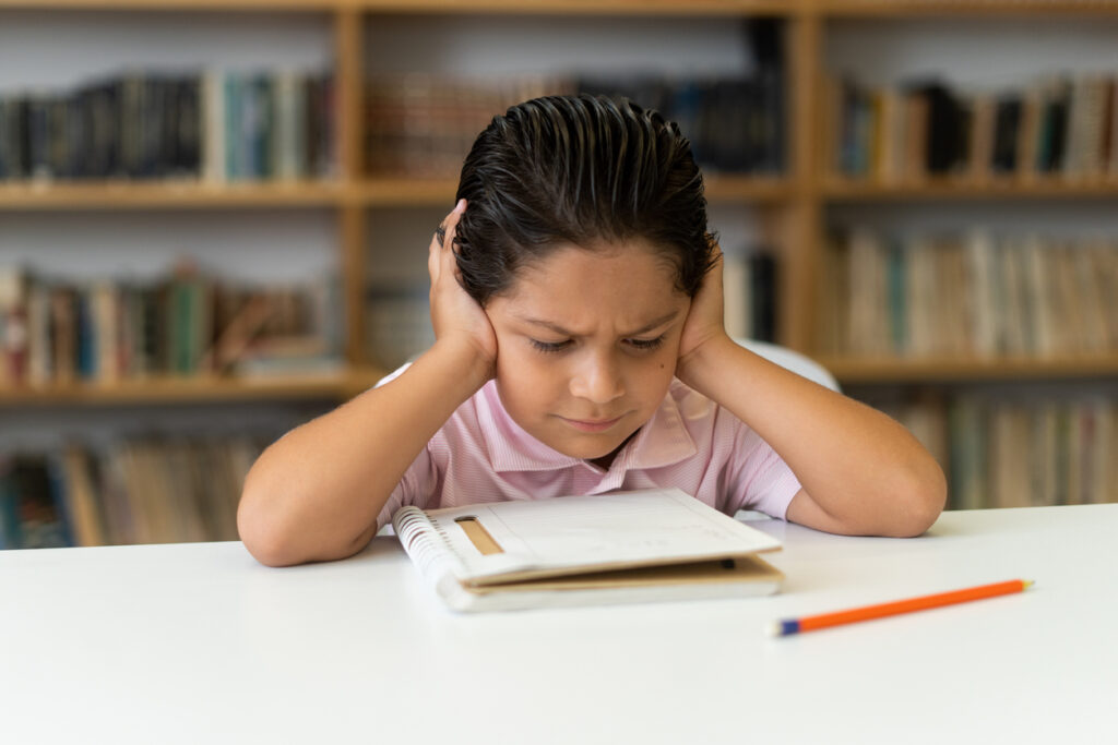 Young student frowning in concentration while studying at a library table.