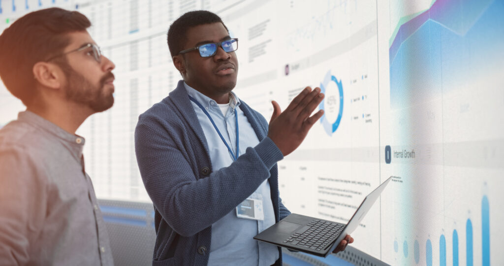 Two professionals discussing performance-based budgeting data on a digital screen with charts and graphs.